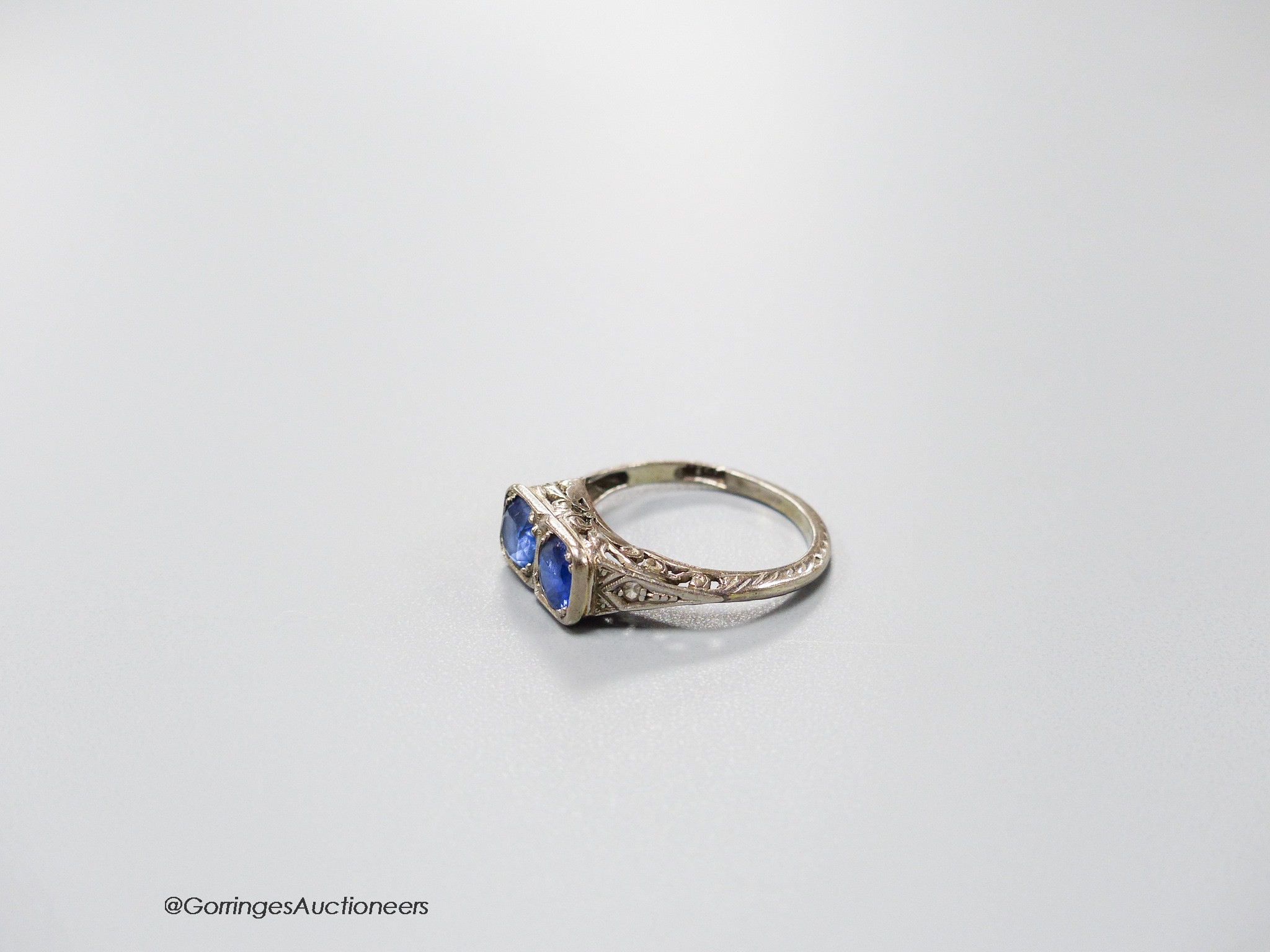 A 1920's white metal (stamped 18ct & plat) and two stone sapphire set ring with carved and single stone diamond chip set shoulders, size K, gross weight 3.2 grams